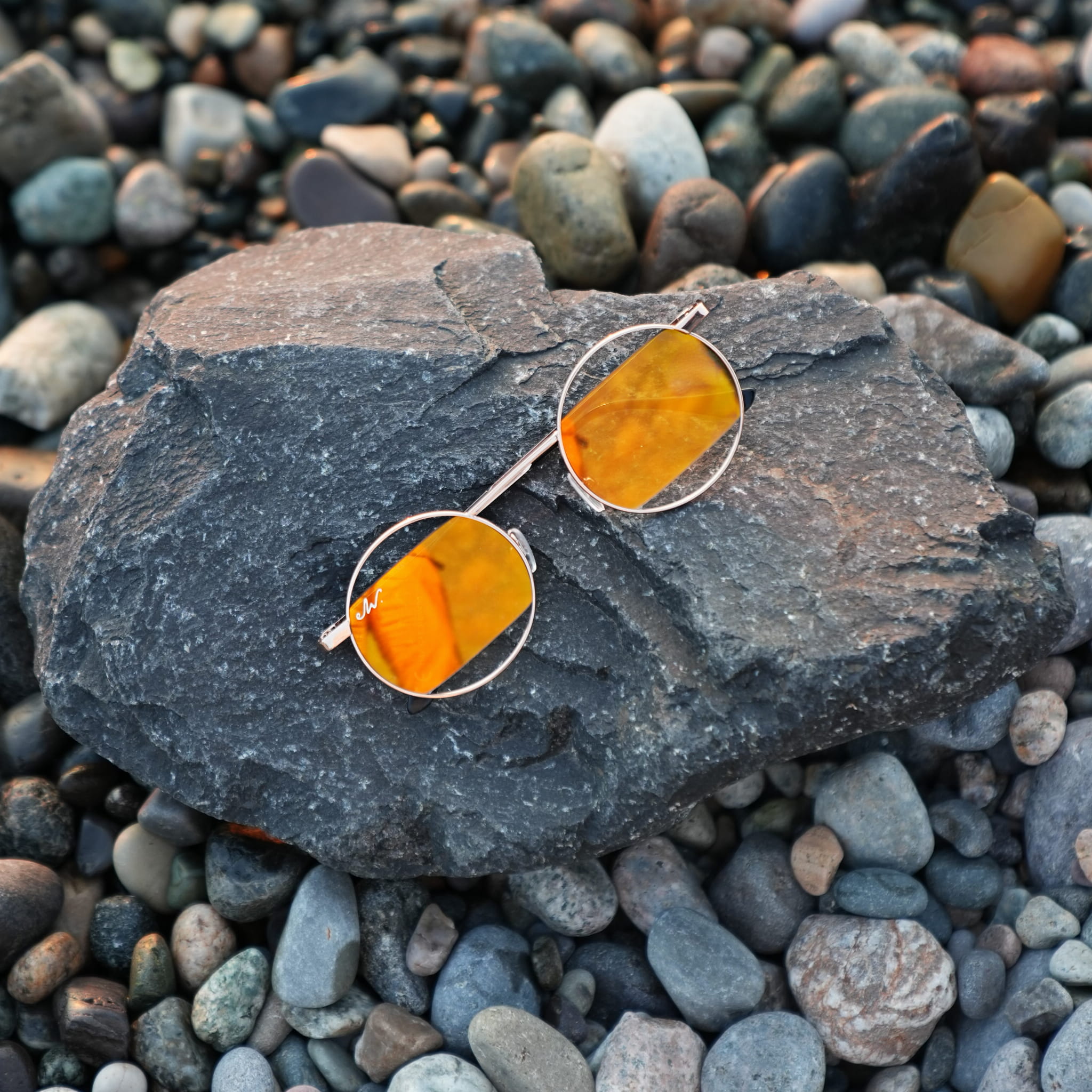 Eleganckie złote okulary Gold Fire z lustrzanymi szkłami ułożone na szarym kamieniu, stylizacja wakacyjna.